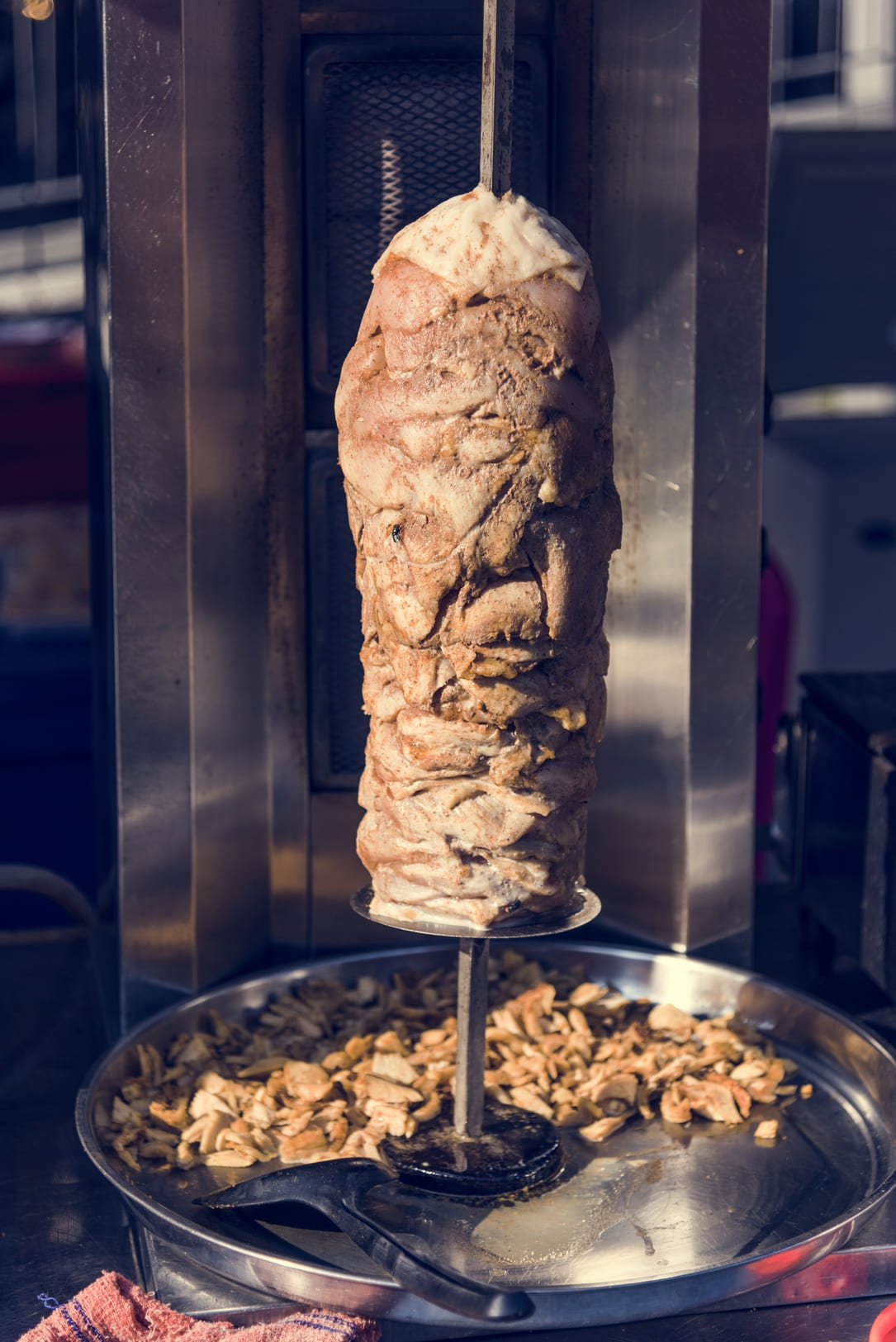 Rollo de carne de kebab en grill apagado. Hay carne ya cortada debajo.