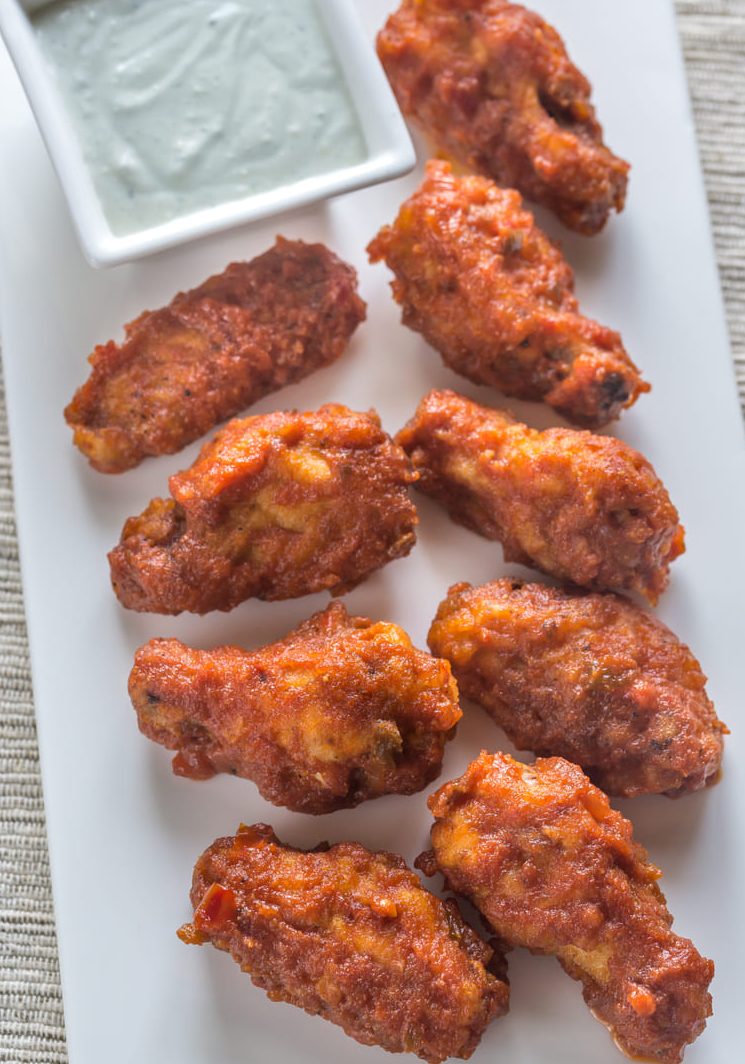 Alitas de pollo fritas acompañadas con salsa yogurt servidas en una bandeja blanca